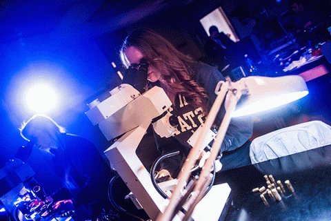 female student looking into a microscope in a darkly lit criminology lab with blue light in the background, and spent bullets on the table on the left.